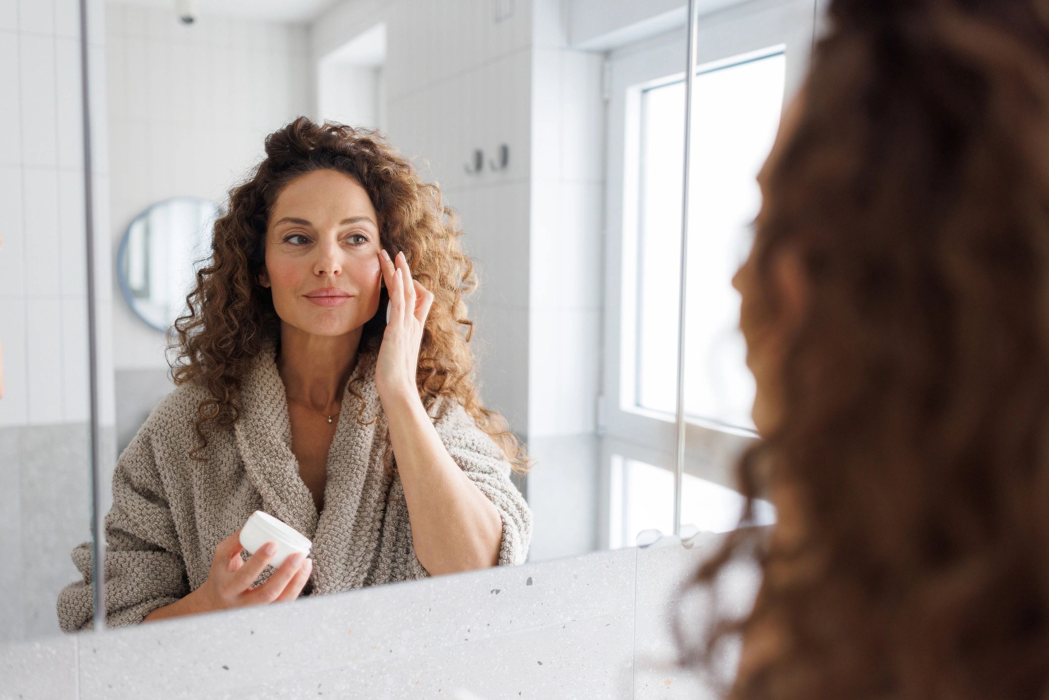 Woman practicing a self-care skincare routine in a bright bathroom